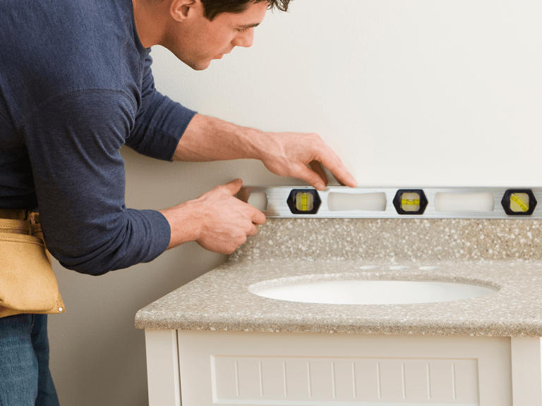 A DIYer using a level when installing a new bathroom countertop.