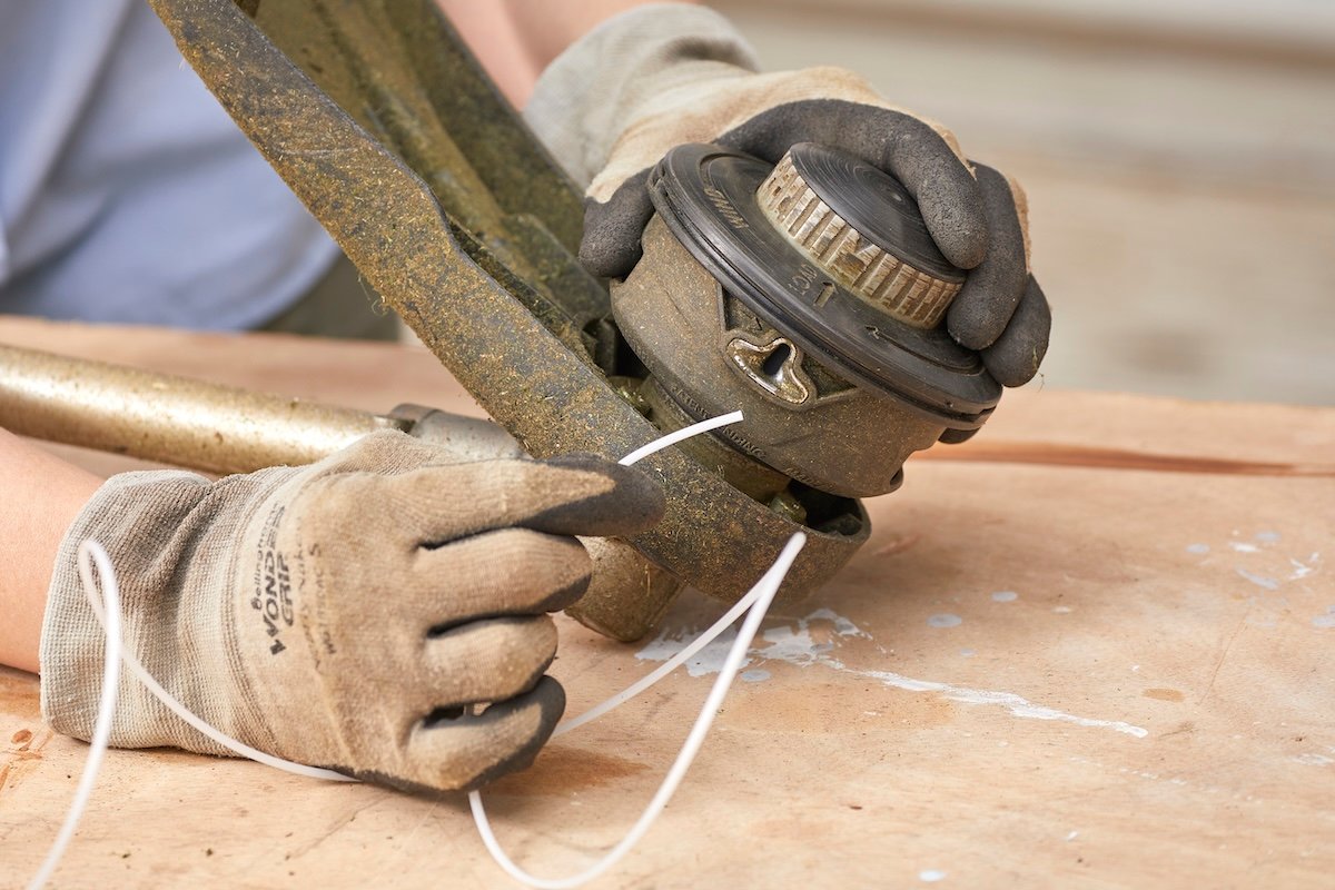 Woman inserts a string into a hole on the side of a string trimmer.