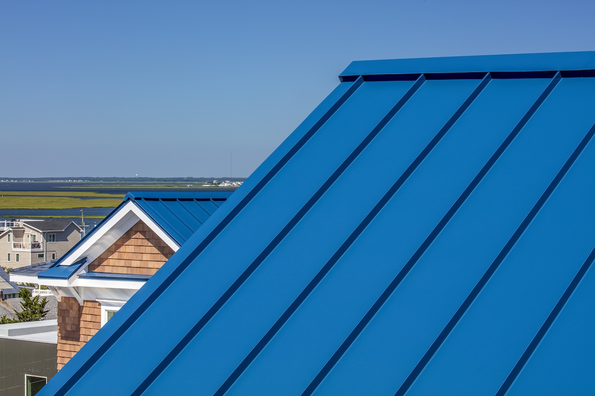 A blue metal roof for energy efficiency on a house near a body of water.