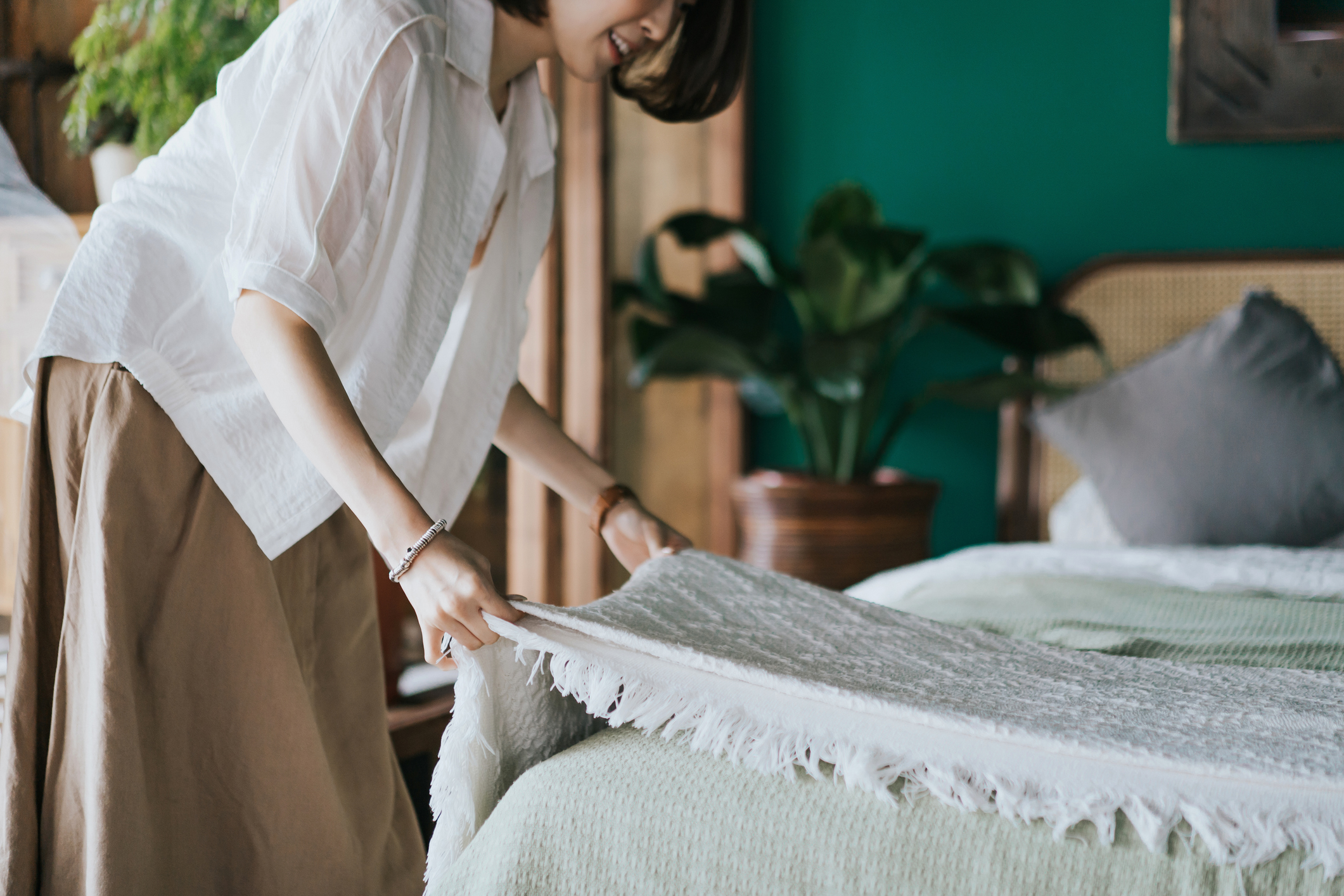 Woman doing her morning routine, making up her bed at home.