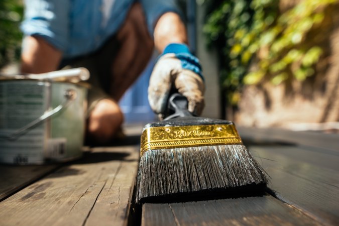 Man holding brush and staining wooden deck a dark brown color.