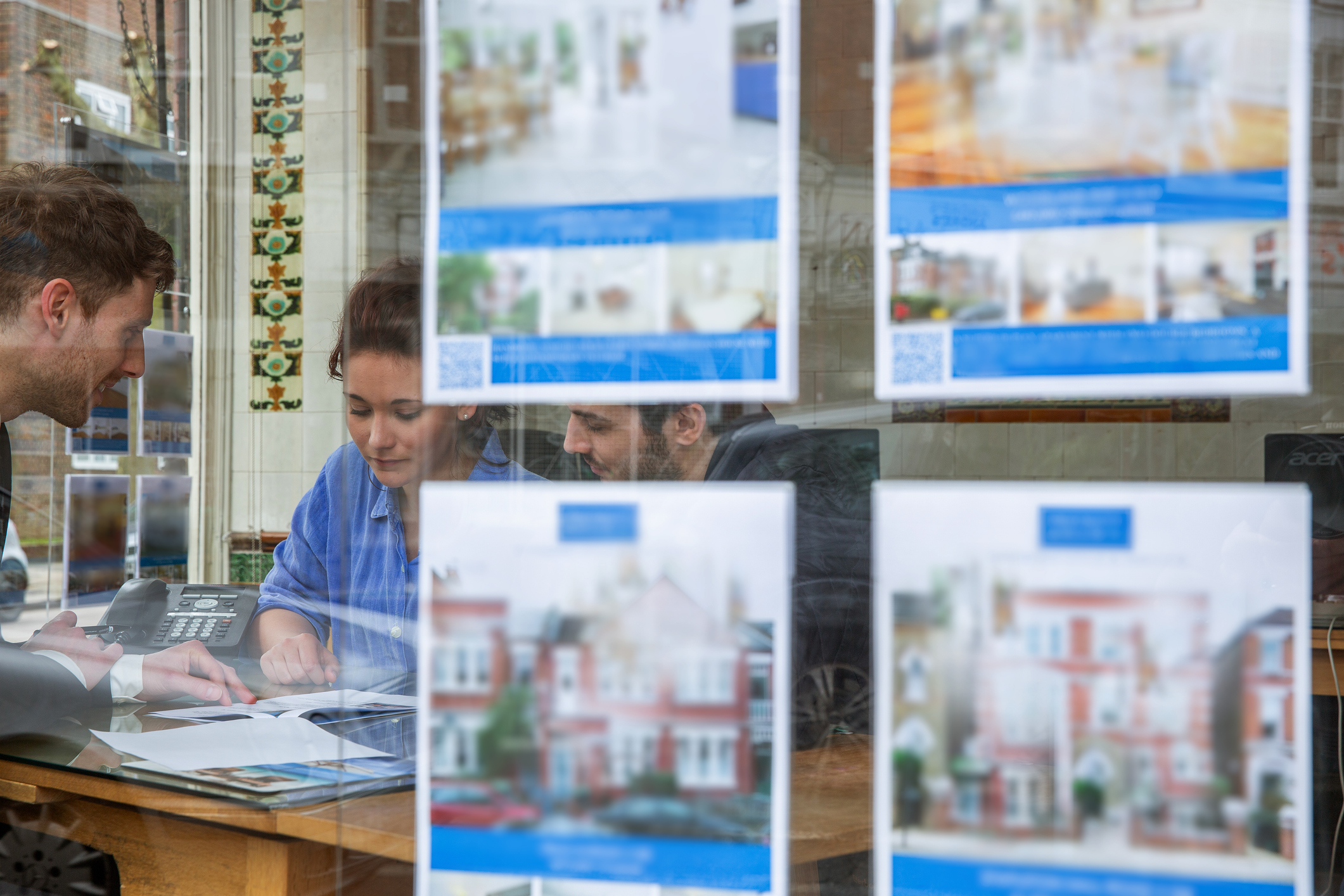 Couple inside real estate office with home listings on window.