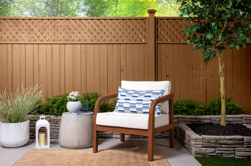 Cedar color stained fence with chair in front of it in backyard.