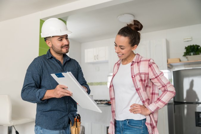 Architect talking to a woman about remodeling her kitchen and showing her the blueprints.