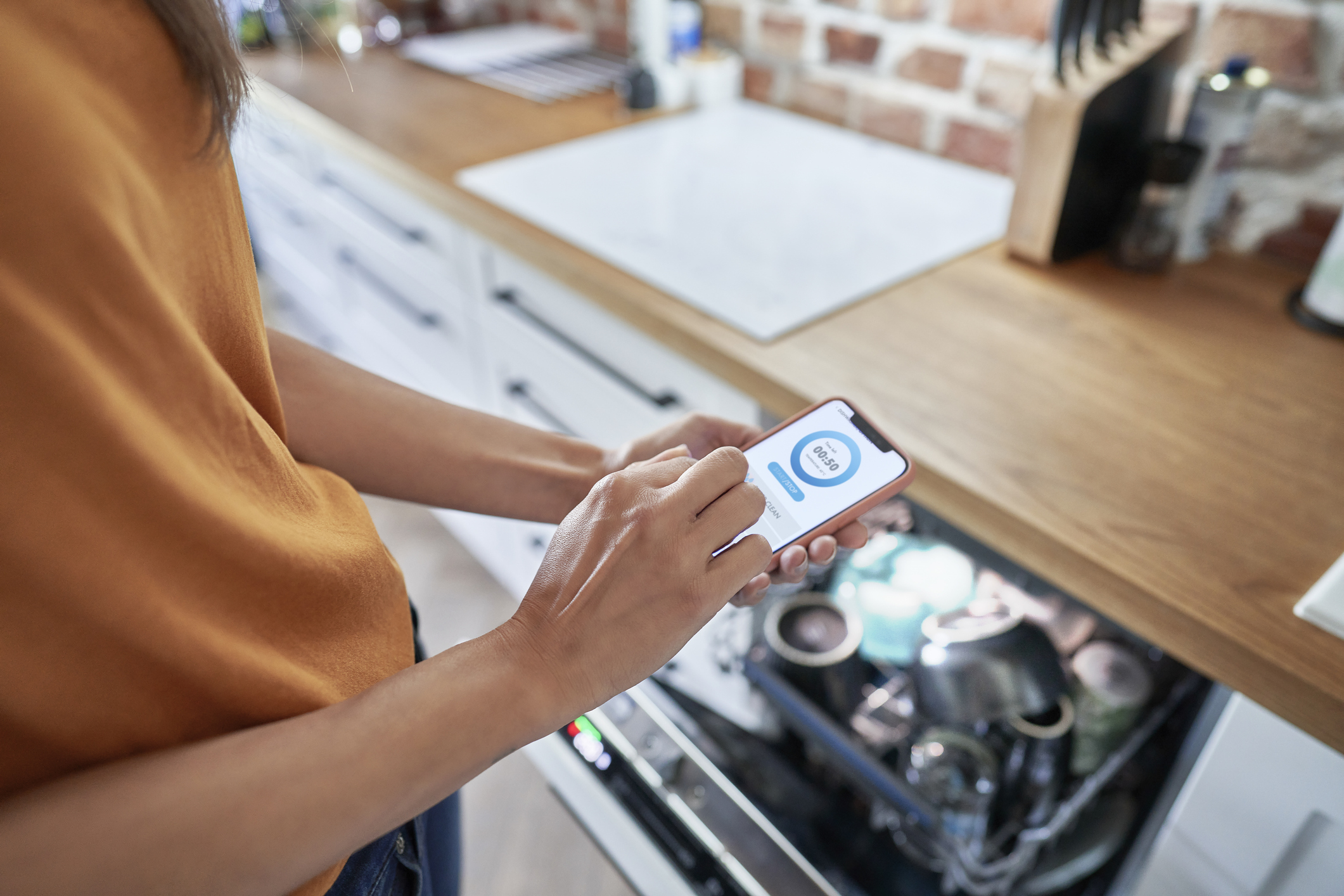 Faceless person using a mobile application to control a dishwasher.