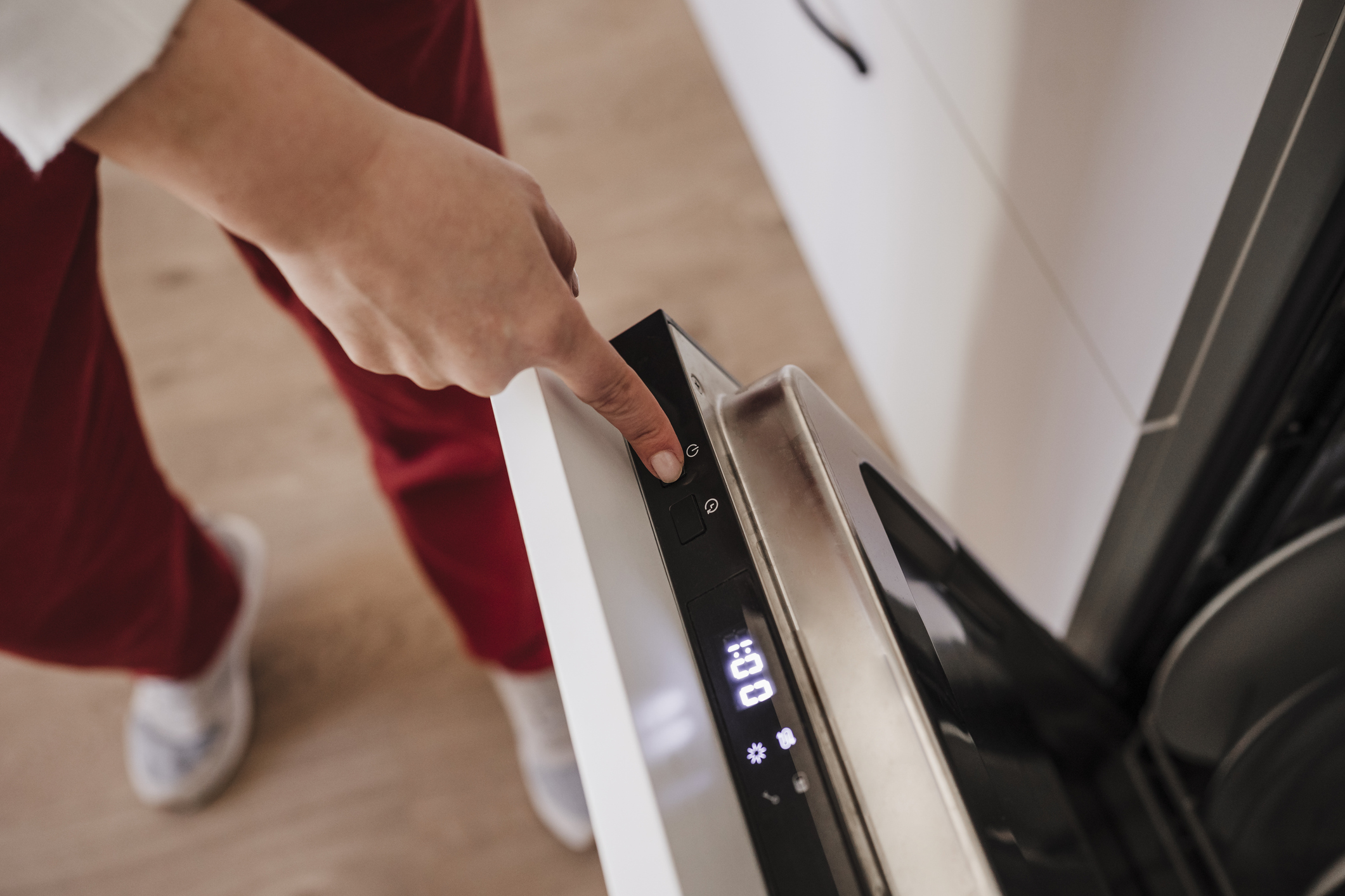Woman turning off dishwasher at home and touching modern screen buttons.