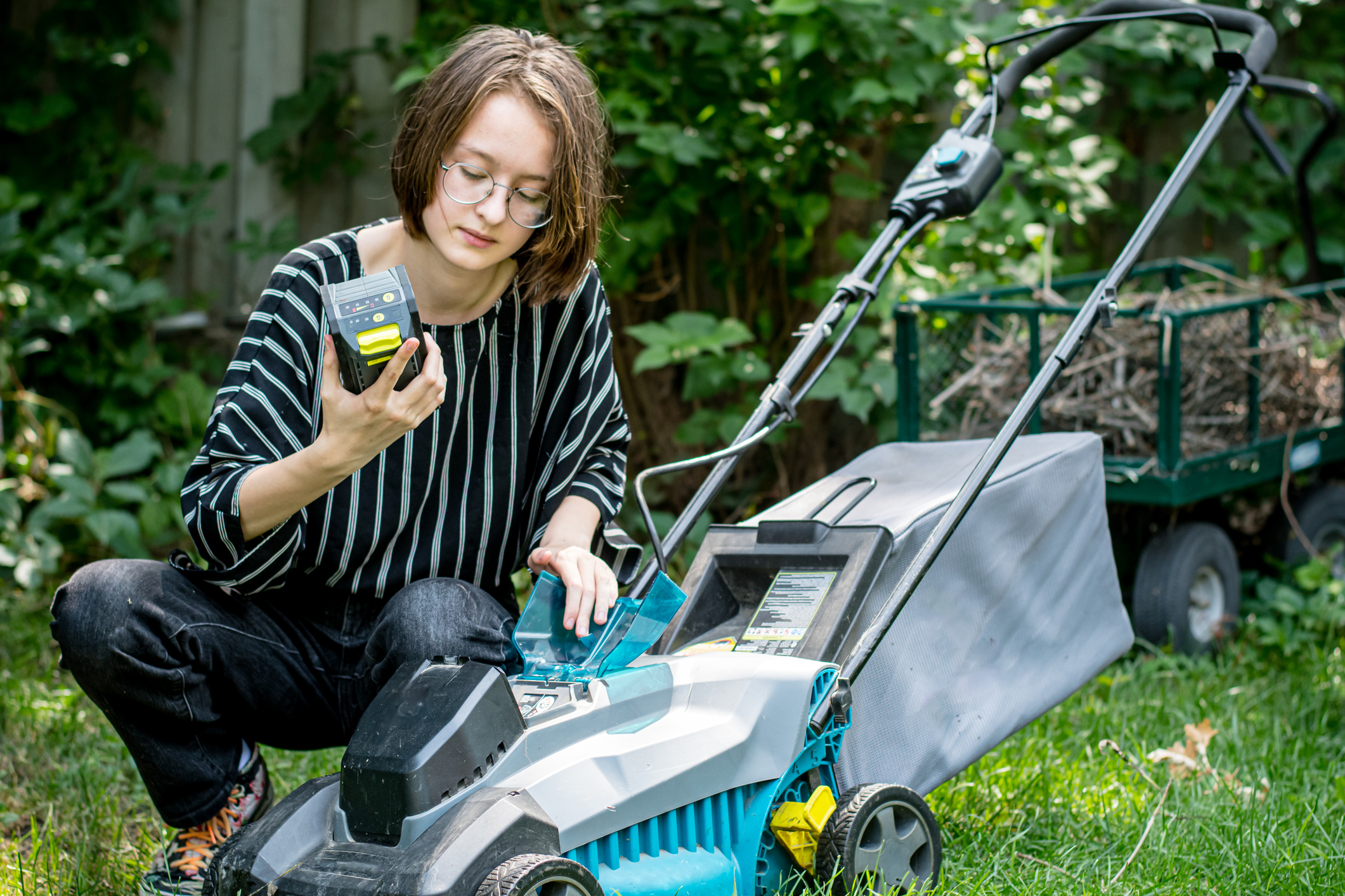 Young woman in backyard inserting a battery into a lawn mower