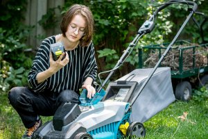 Young woman in backyard inserting a battery into a lawn mower