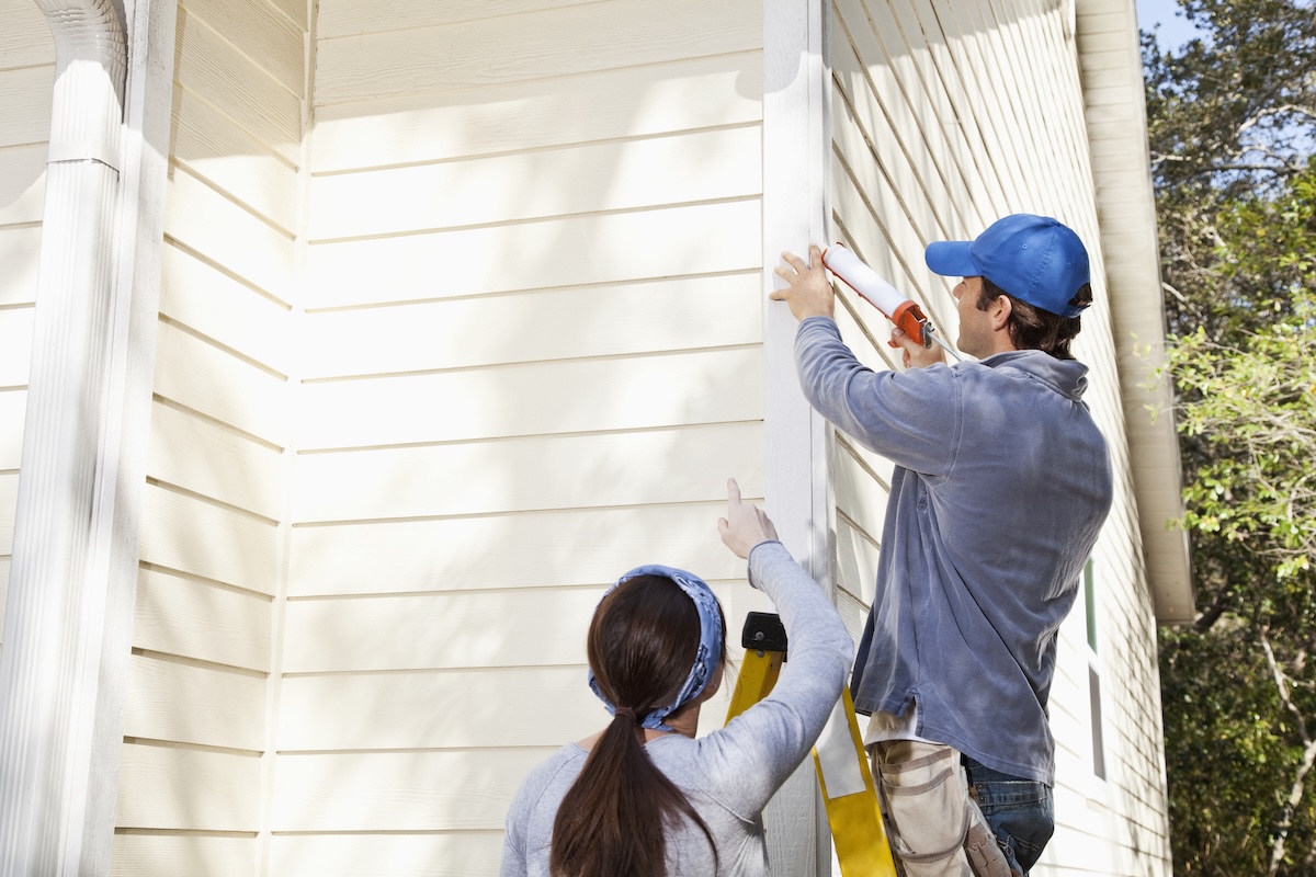 Homeowners caulking the siding on their house.