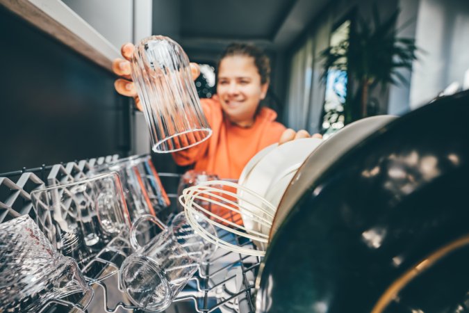 Smiling young woman putting a glass in a dishwasher. View from inside dishwasher.