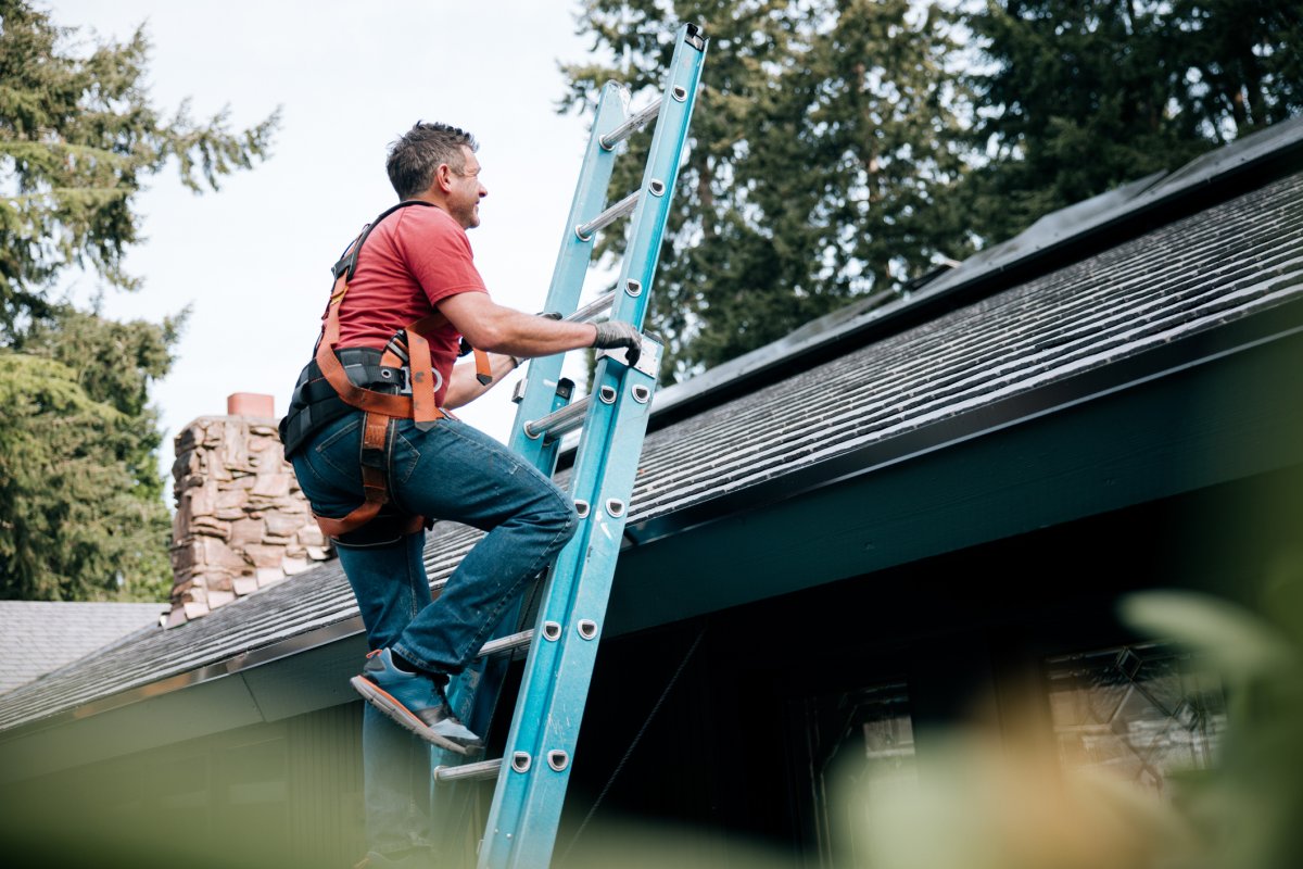 A man climbing a ladder to inspect the roof of a house.