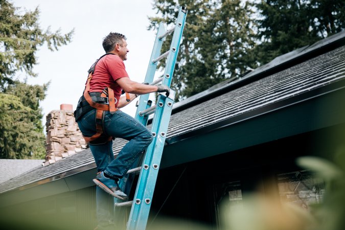 A man climbing a ladder to inspect the roof of a house.