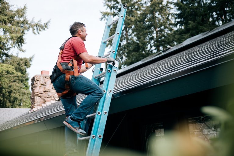 A man climbing a ladder to inspect the roof of a house.