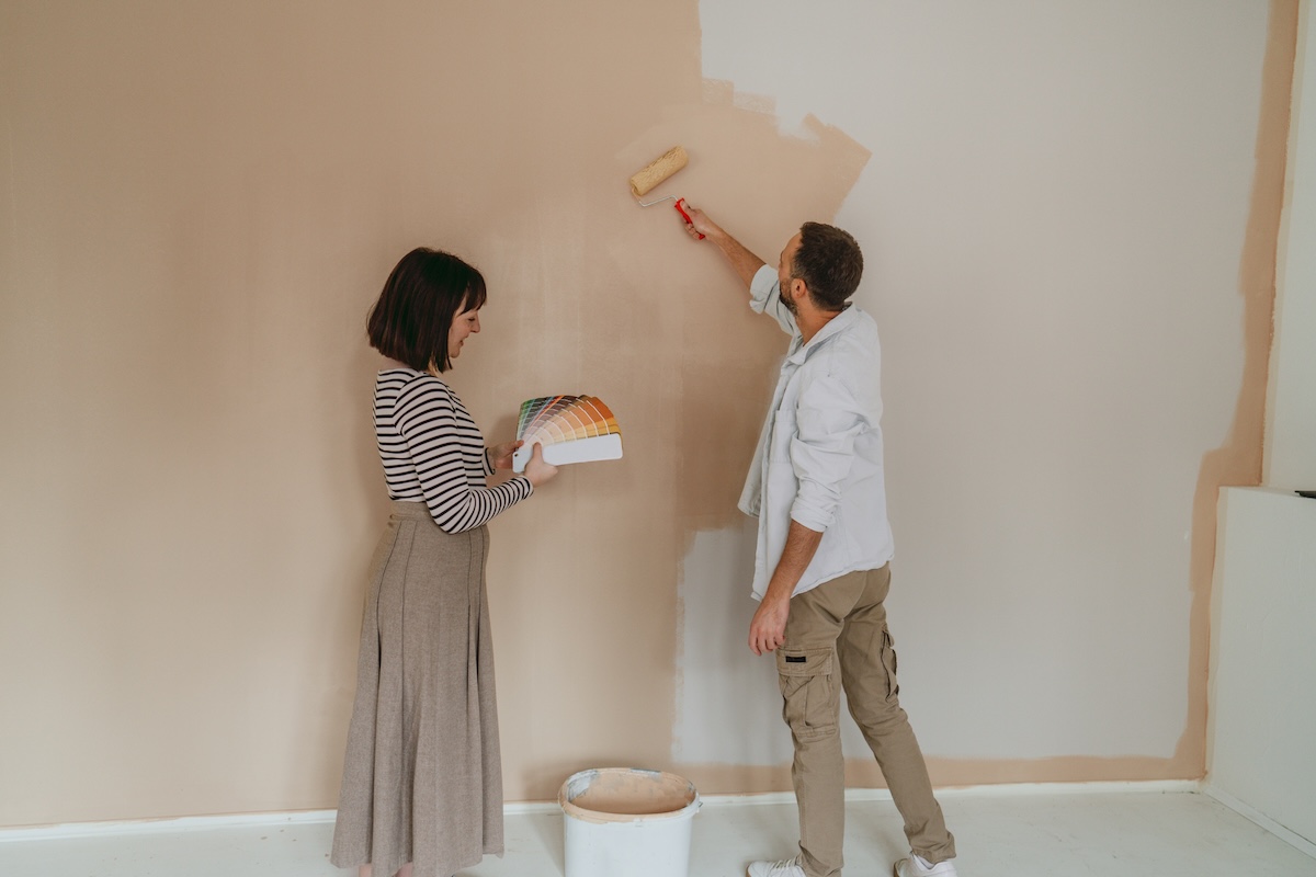 A designer and contractor painting a wall beige and looking at paint fan deck.