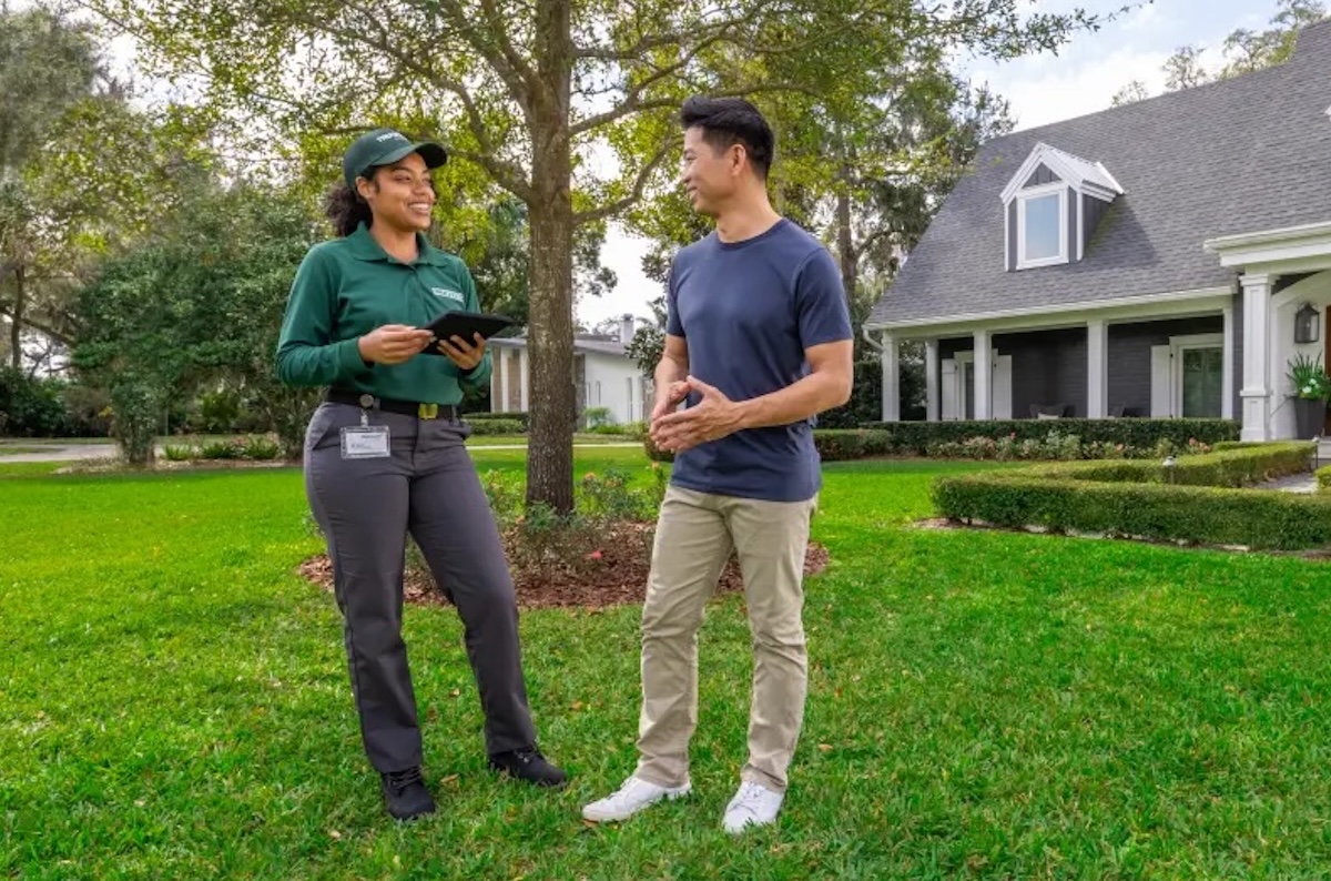 A TruGreen representative consults with a male homeowner on his front lawn.