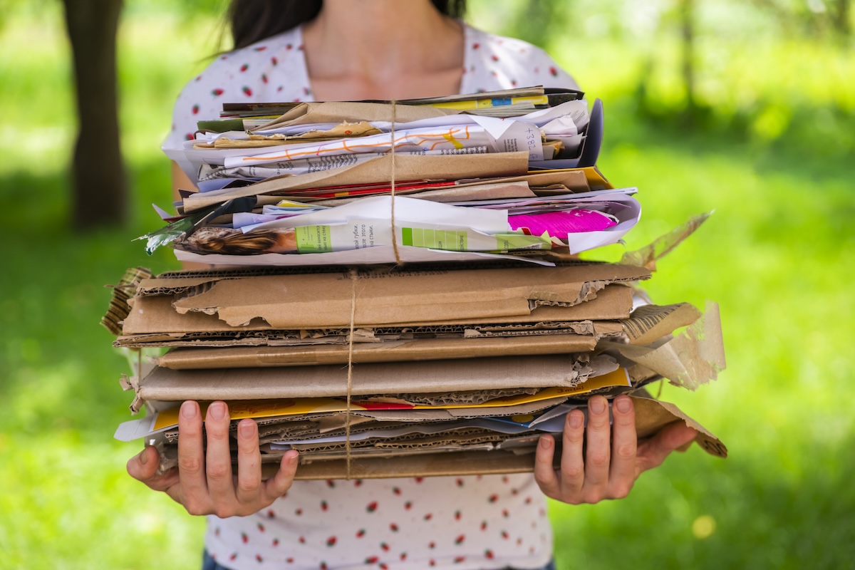 A woman holding a stack of cardboard outside.