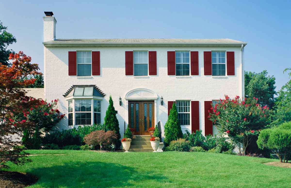 White brick house with red shutters and foundation plants in the front yard