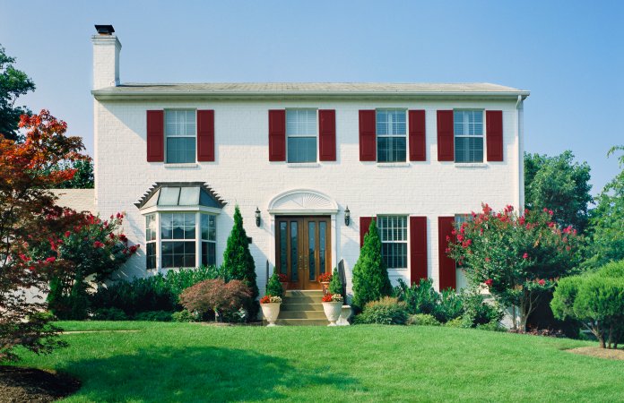 White brick house with red shutters and foundation plants in the front yard