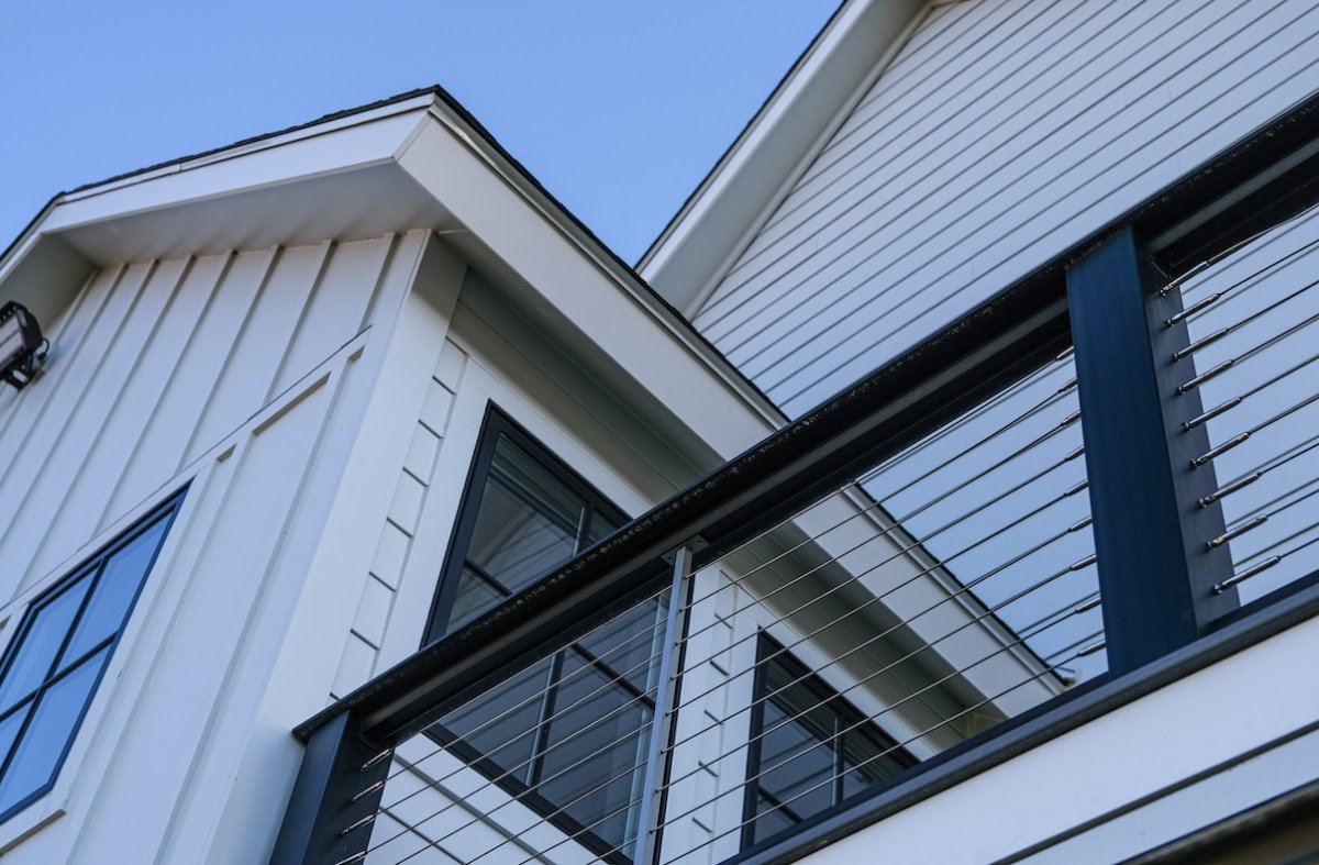A modern farmhouse clad in white James Hardie siding with black second-story deck railings.