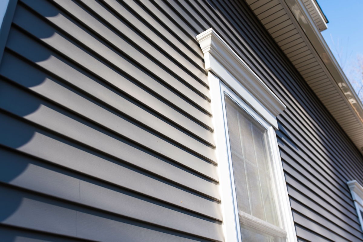 Low view looking toward second floor of house clad in grey vinyl siding.