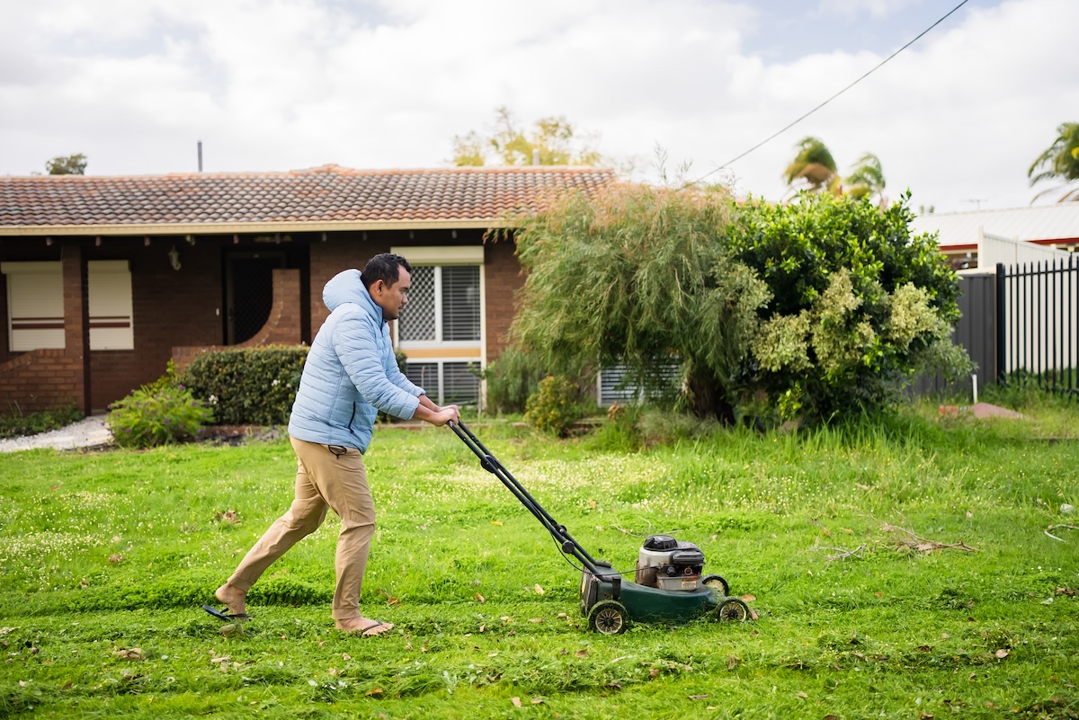 A man mows a wet lawn in front of his house.