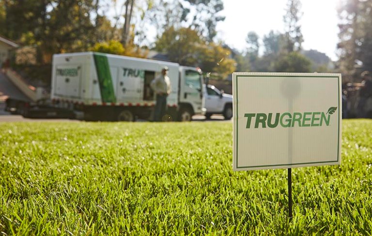 TruGreen truck parked in front of a lush lawn with a TruGreen sign placed in the lawn.