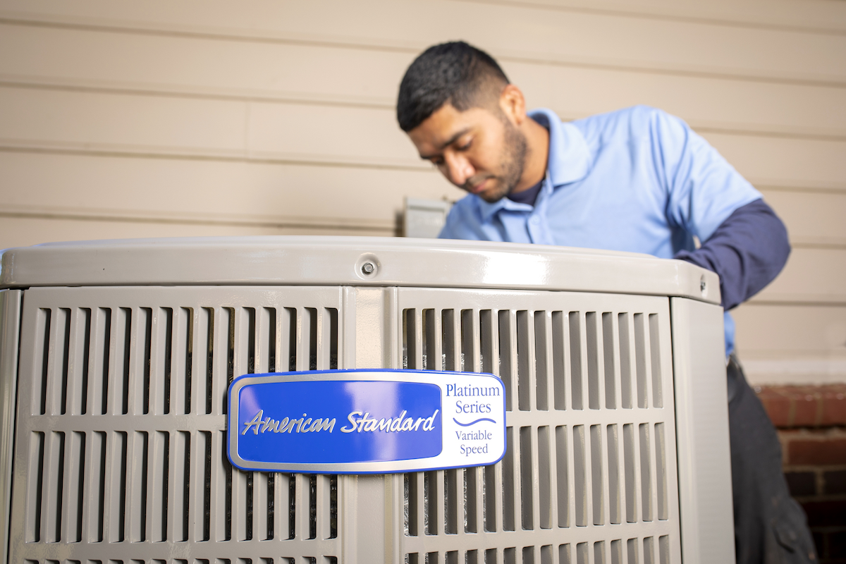 An American Standard HVAC technician installing a heat pump outside of a home.