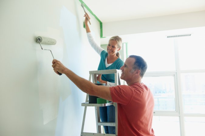 Smiling woman and man painting an interior wall.