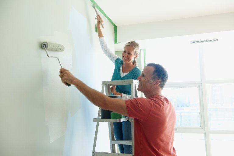 Smiling woman and man painting an interior wall.