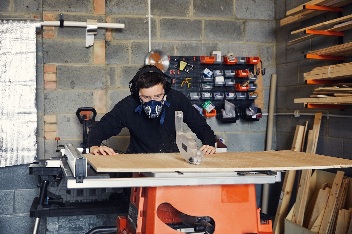 A woodworker using a table saw with PPE and saw guards.