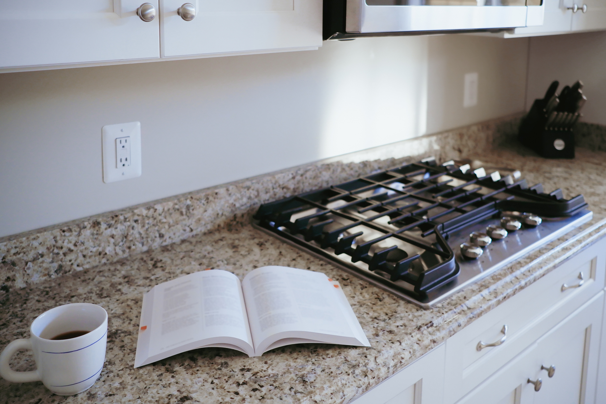 Close-up of an open cookbook on kitchen counter next to a stove.