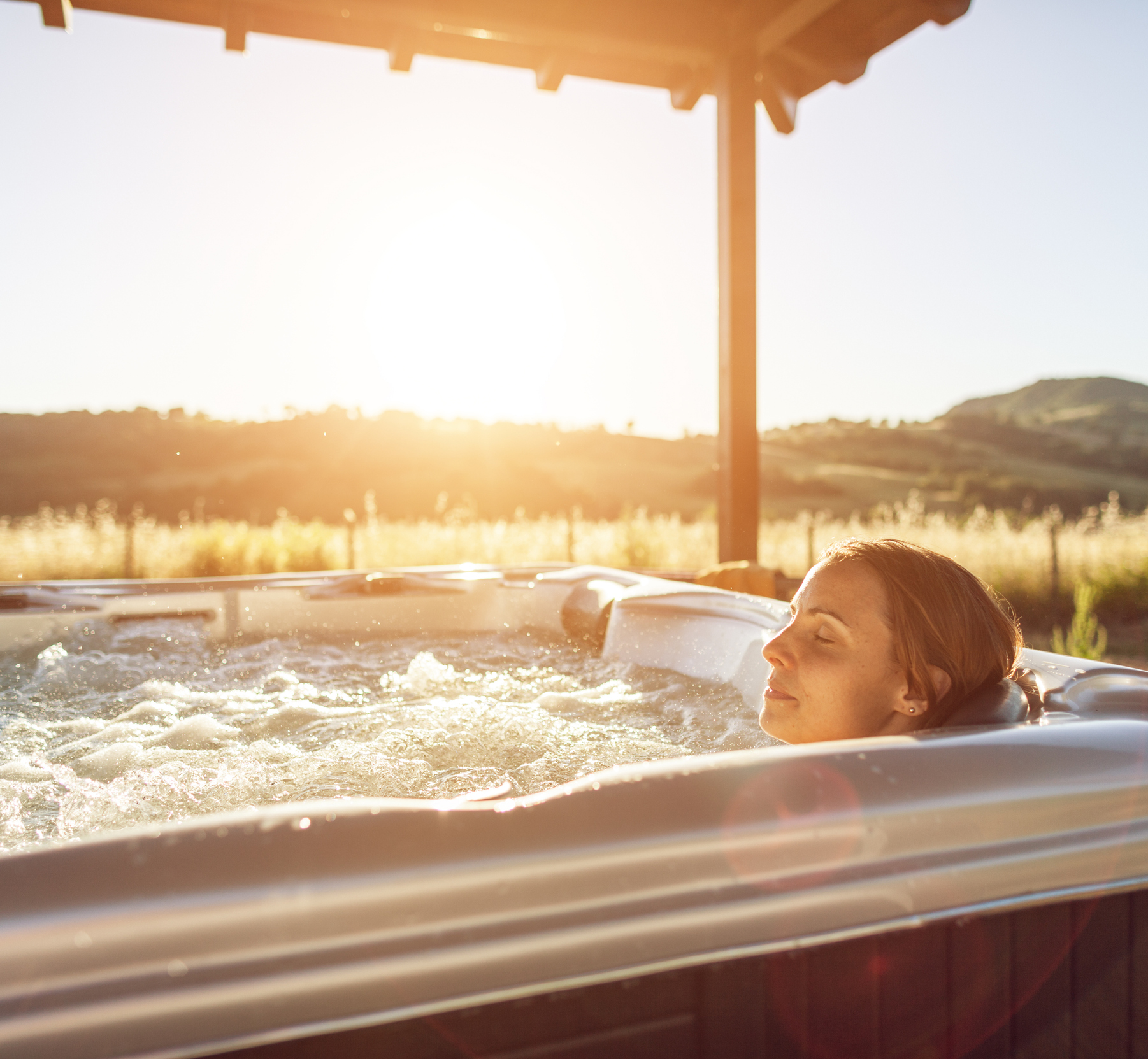 Happy and relaxed woman in whirlpool hot tub at sunset.