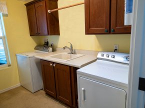 A laundry room with washing machine, clothes dryer, utility sinks, and brown cabinets.