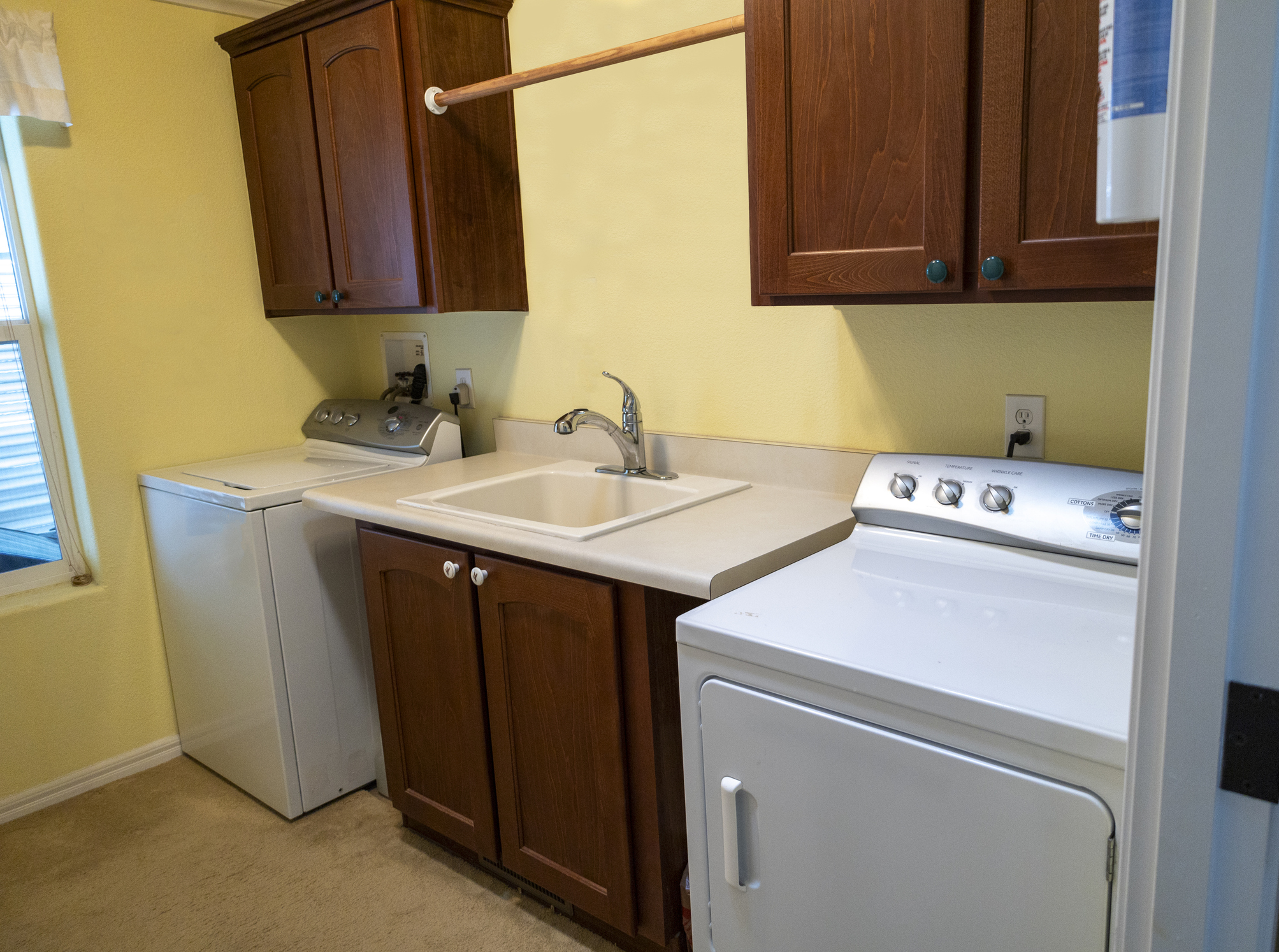 A laundry room with washing machine, clothes dryer, utility sinks, and brown cabinets.