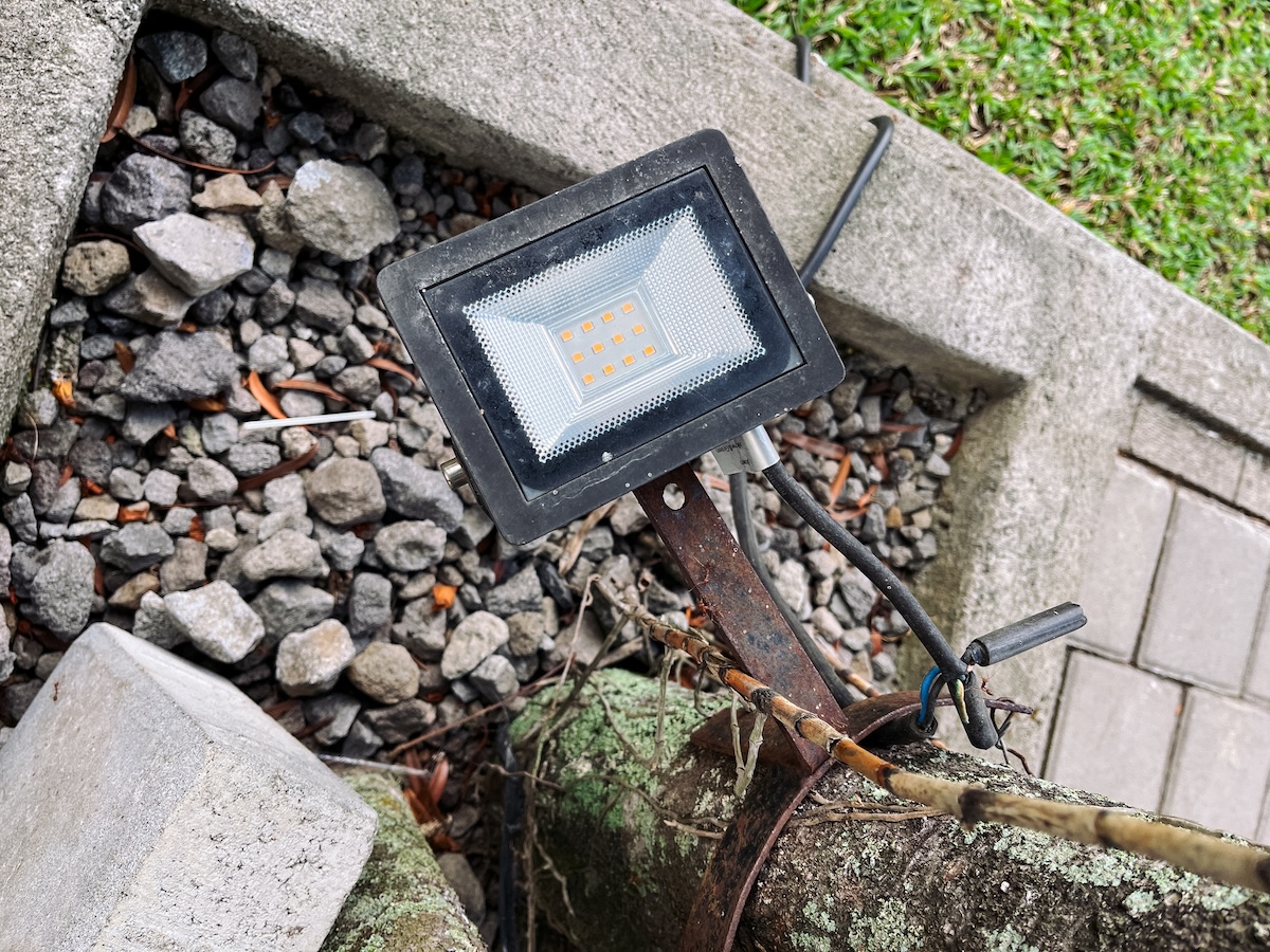 A broken outdoor light with rust and exposed wires.