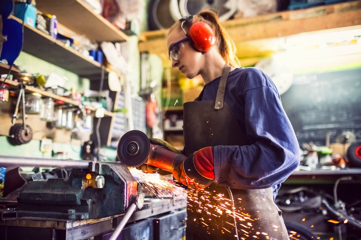 A DIYer using an angle grinder to cut metal in her home workshop.