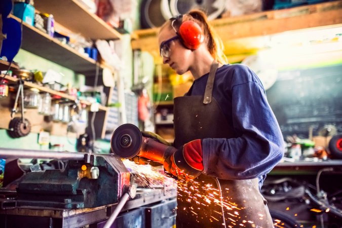 A DIYer using an angle grinder to cut metal in her home workshop.