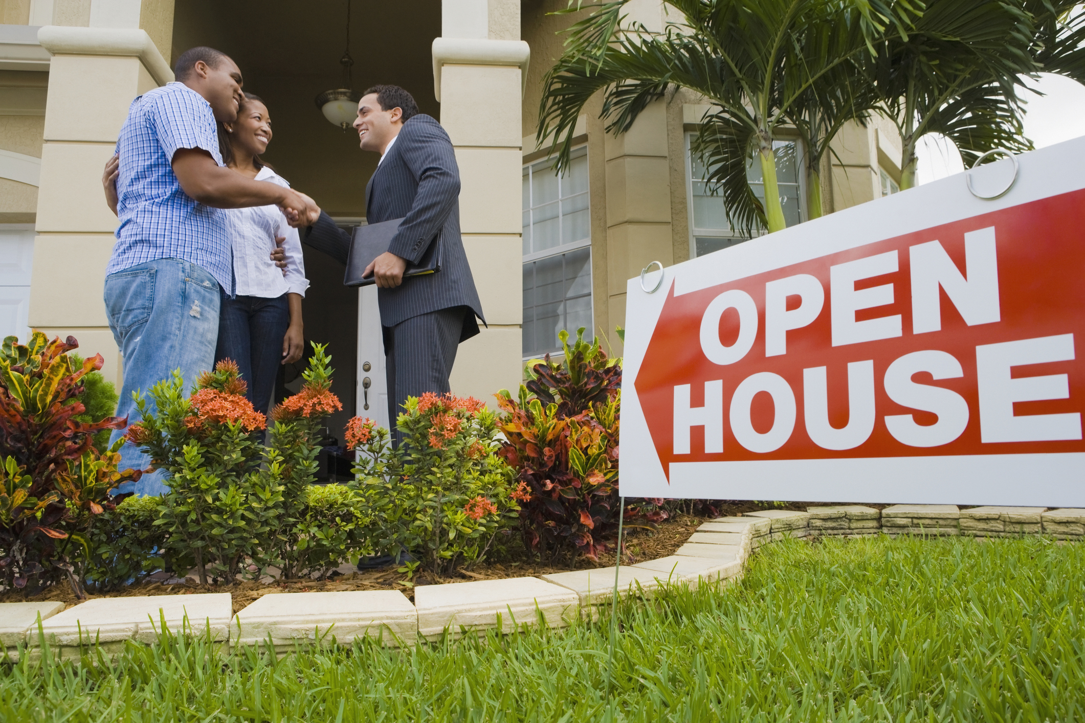 Couple and their realtor looking at a house for sale with an open house sign out front.