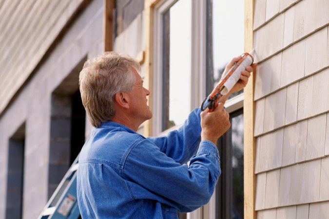 Older man caulking the exterior of a window.