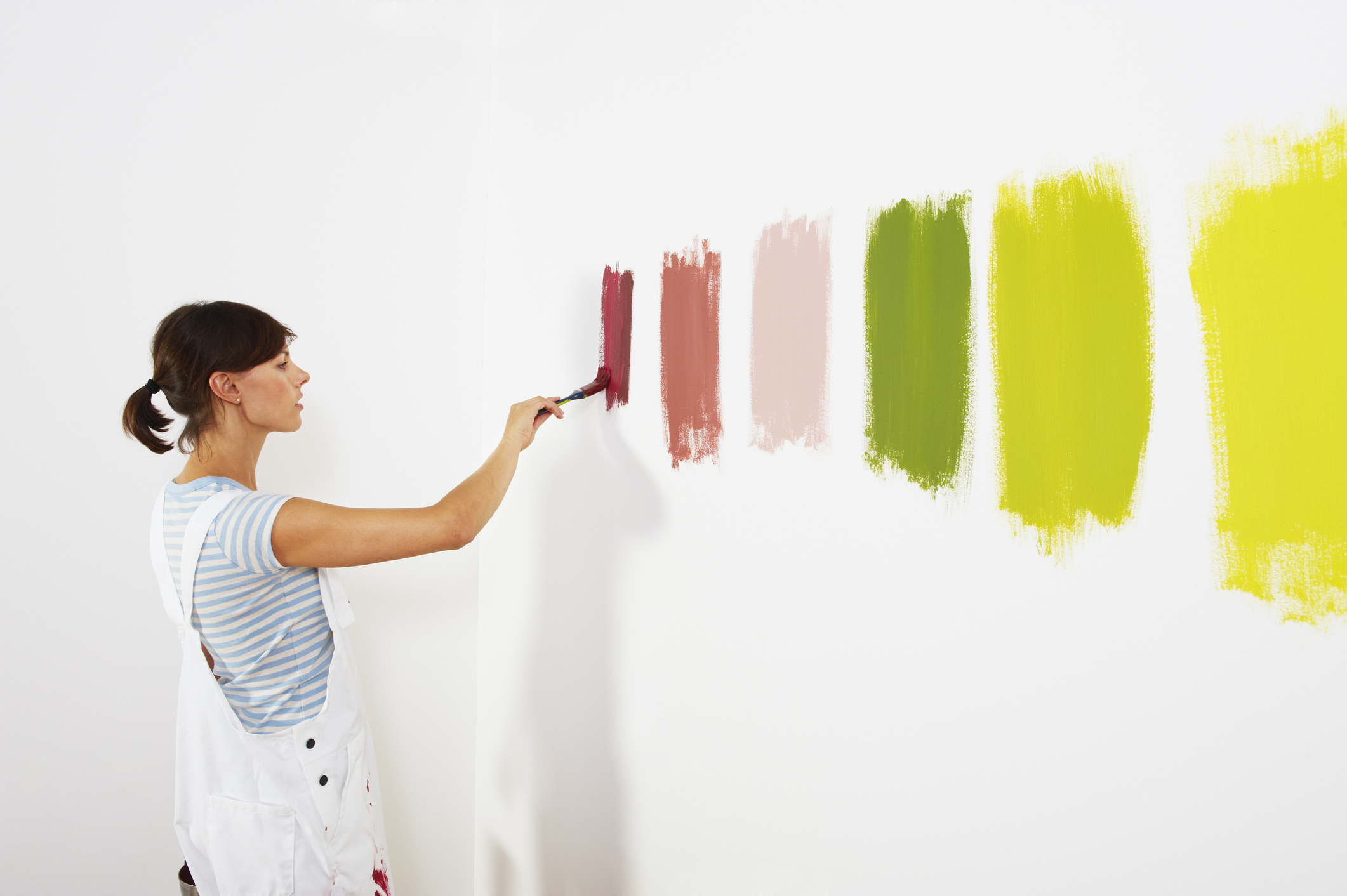 Woman painting green, pink, and red paint samples on the wall.