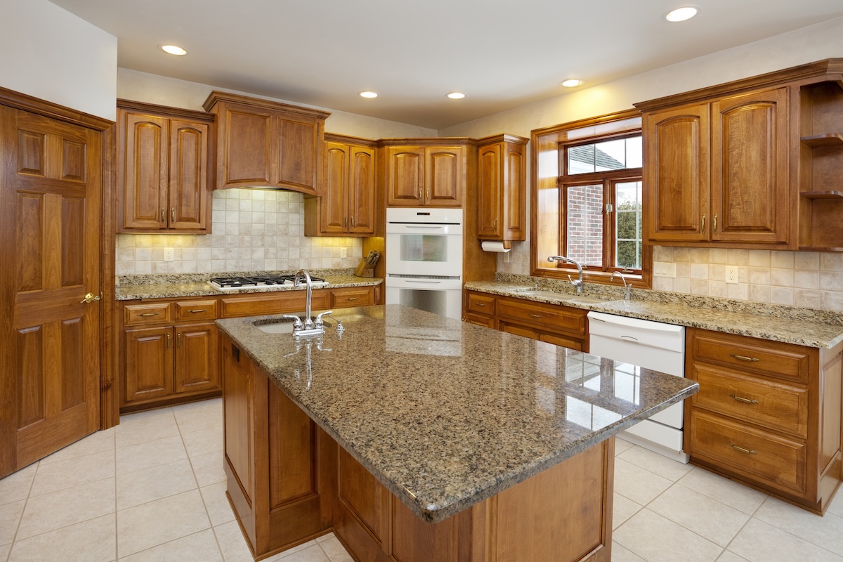 Spacious kitchen with brown granite countertops, medium-toned wood cabinets with arched upper panels, and light colored floors.
