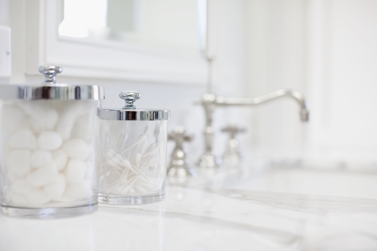 Clear jars with silver lids on a bathroom container with cotton balls.