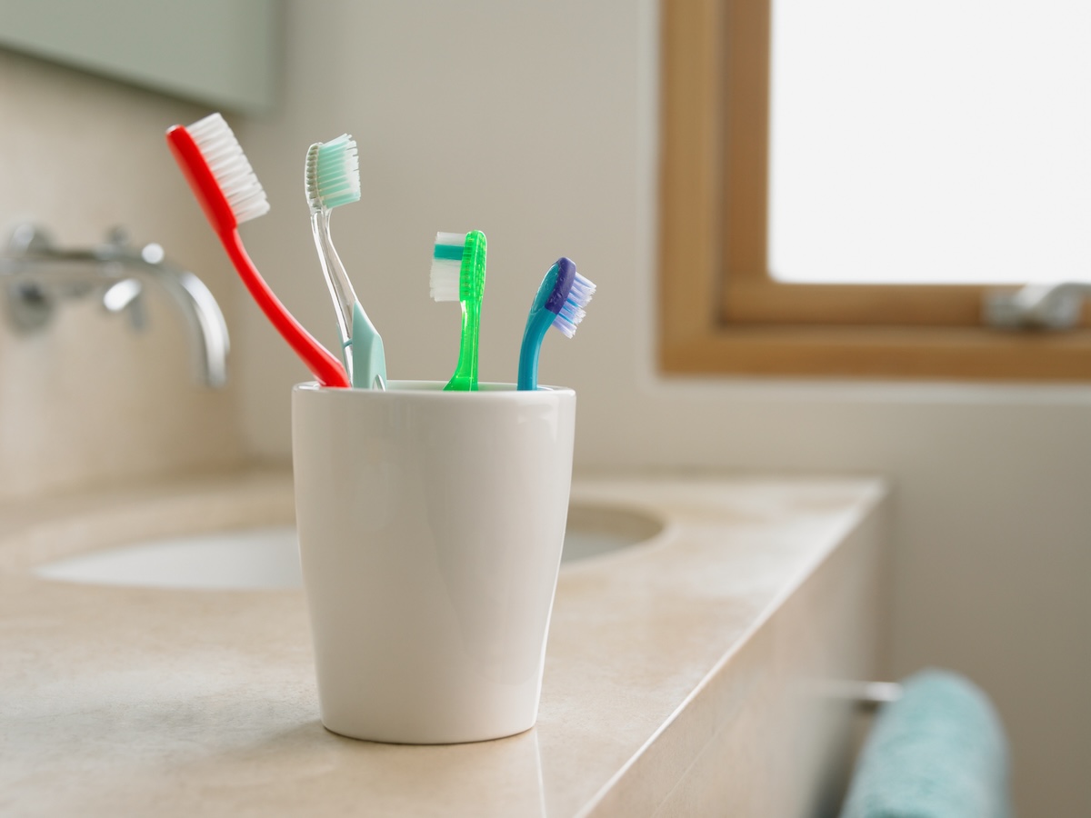 Four multi-colored tooth brushes in a cup by the sink.