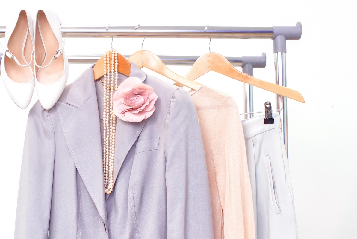 Stylish female outfit hanging on a rail. Women's clothing gray, pink, beige ready to wear on a white background.