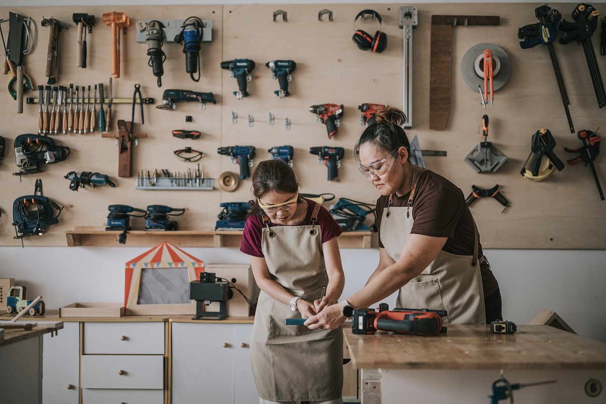 A mother and daughter wear safety goggles while working in a garage together.
