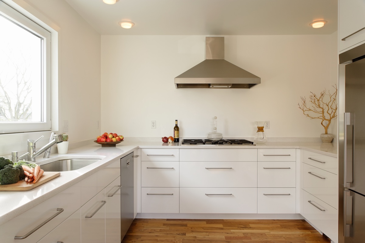 Modern kitchen with stainless range hood and flat-front white lower kitchen cabinets.