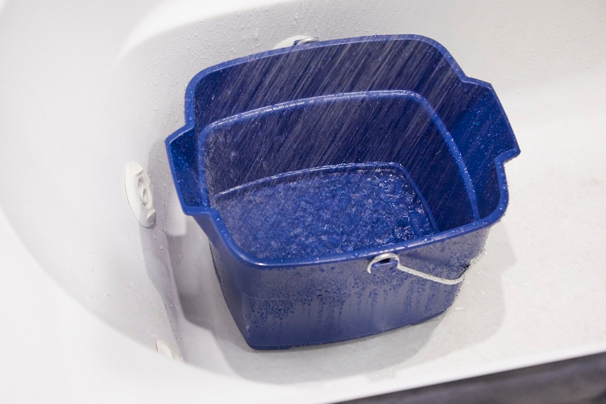 A large blue bucket is in a bathtub collecting water from a running shower.