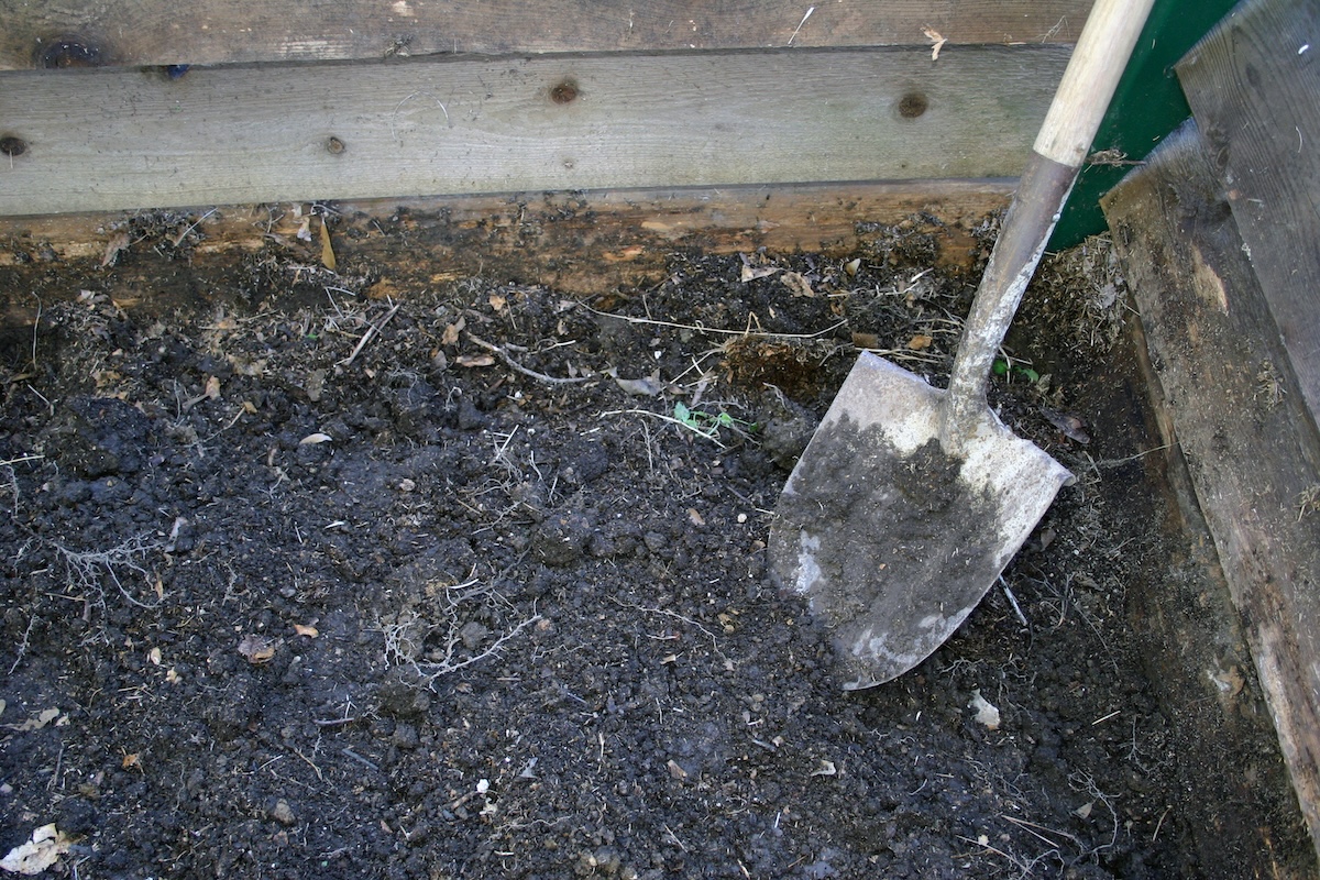 A garden shovel sits in a composting pin.