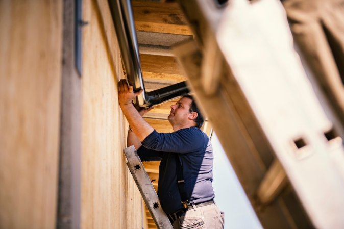 A man installs a rain gutter to the exterior of a home.