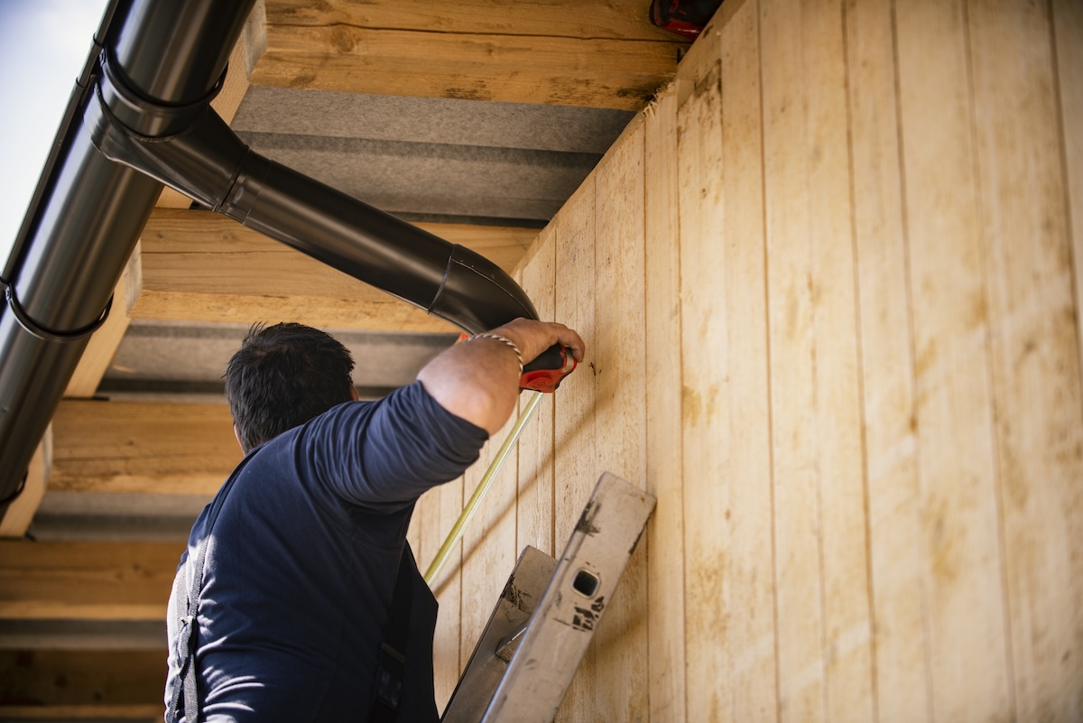 A repair person measures a rain gutter using a tape measure.